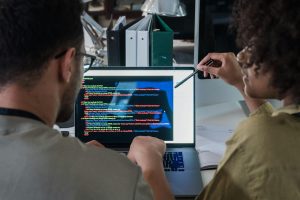 Two developers engage in software programming on a laptop in a modern office setting.