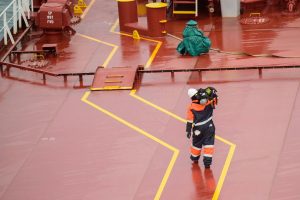 Workers on a cargo ship deck during daytime, wearing protective gear, ensuring safety compliance.